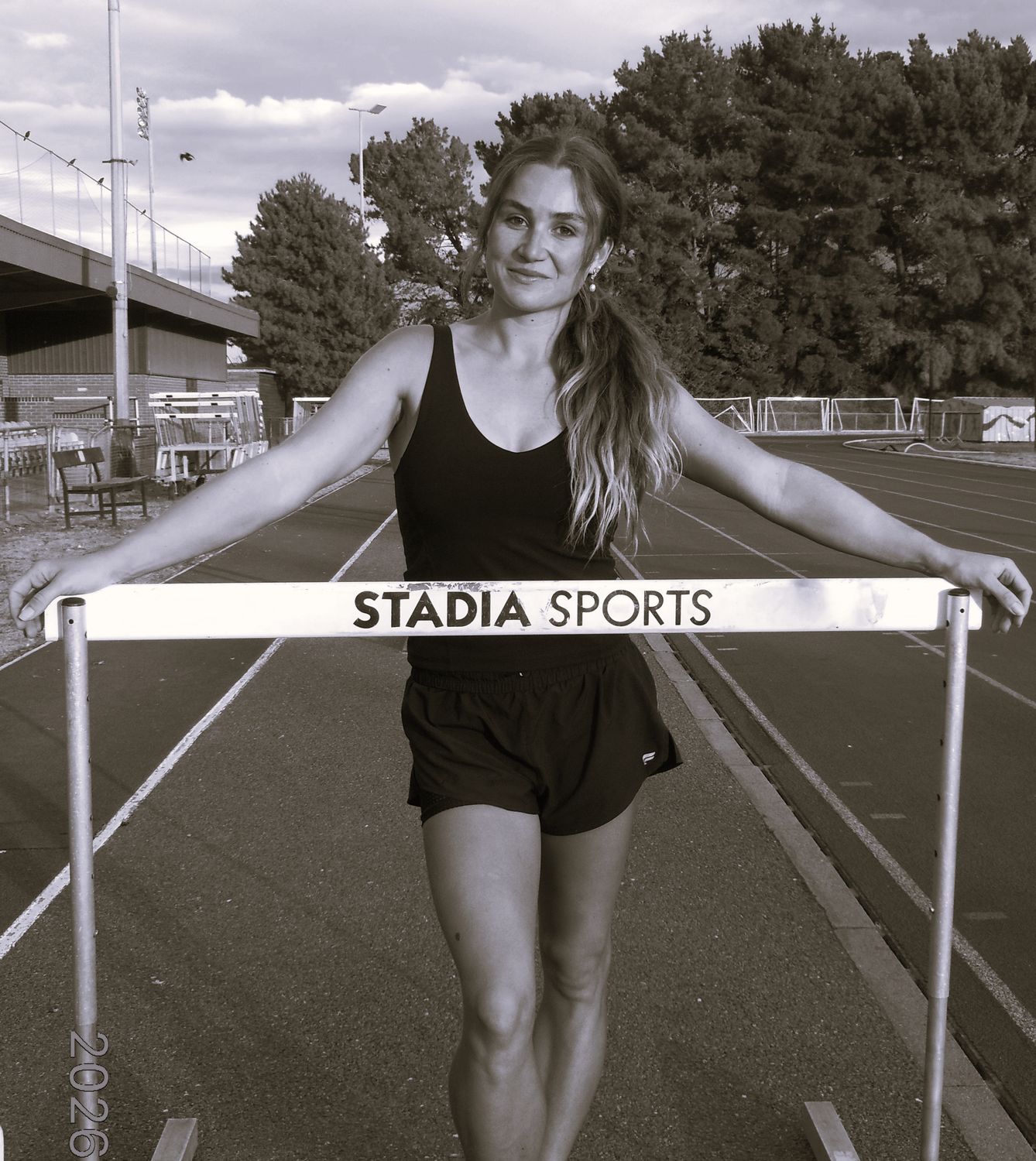 Pippa Earley standing at a hurdle on the track, in black and white